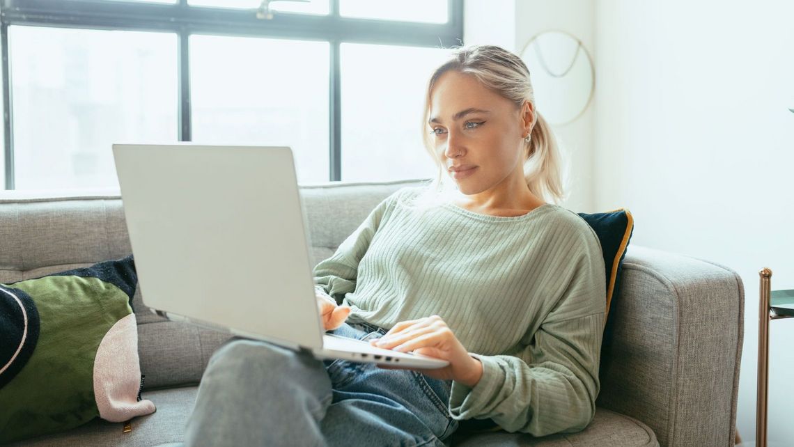 Eine Frau sitzt auf einer Couch und benutzt einen Laptop.