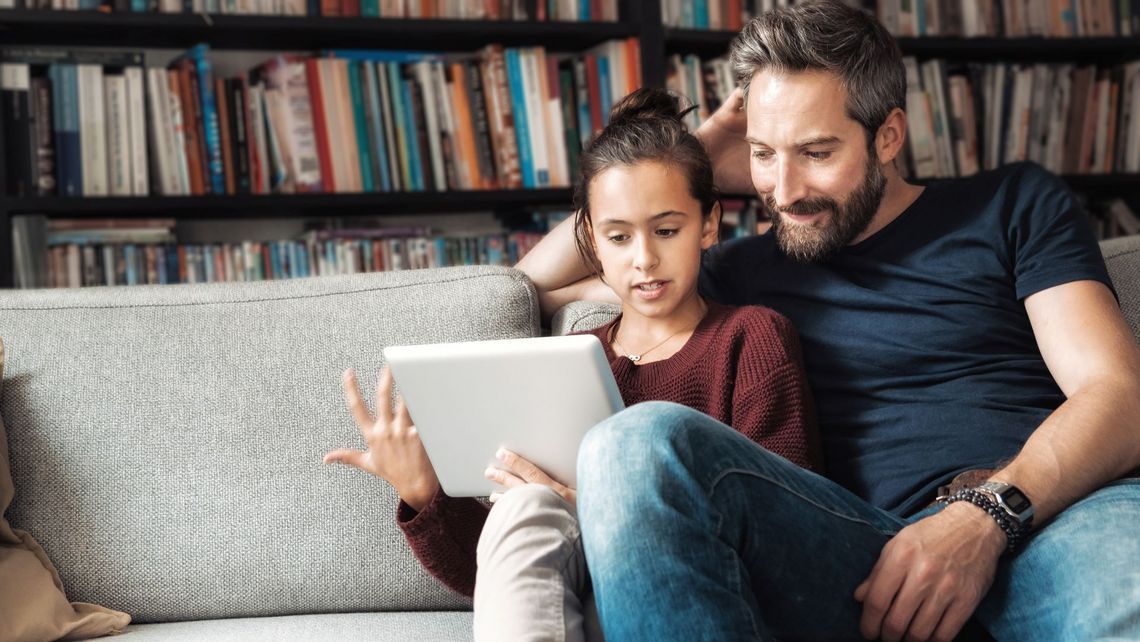 Ein Mann und ein junges Mädchen sitzen auf einer Couch mit einem Tablet.